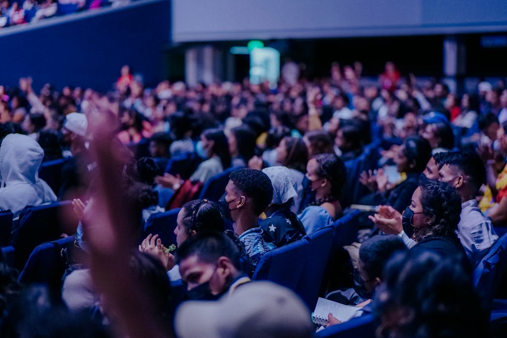 A large, diverse audience attentively watching a live event indoors, seated in rows.