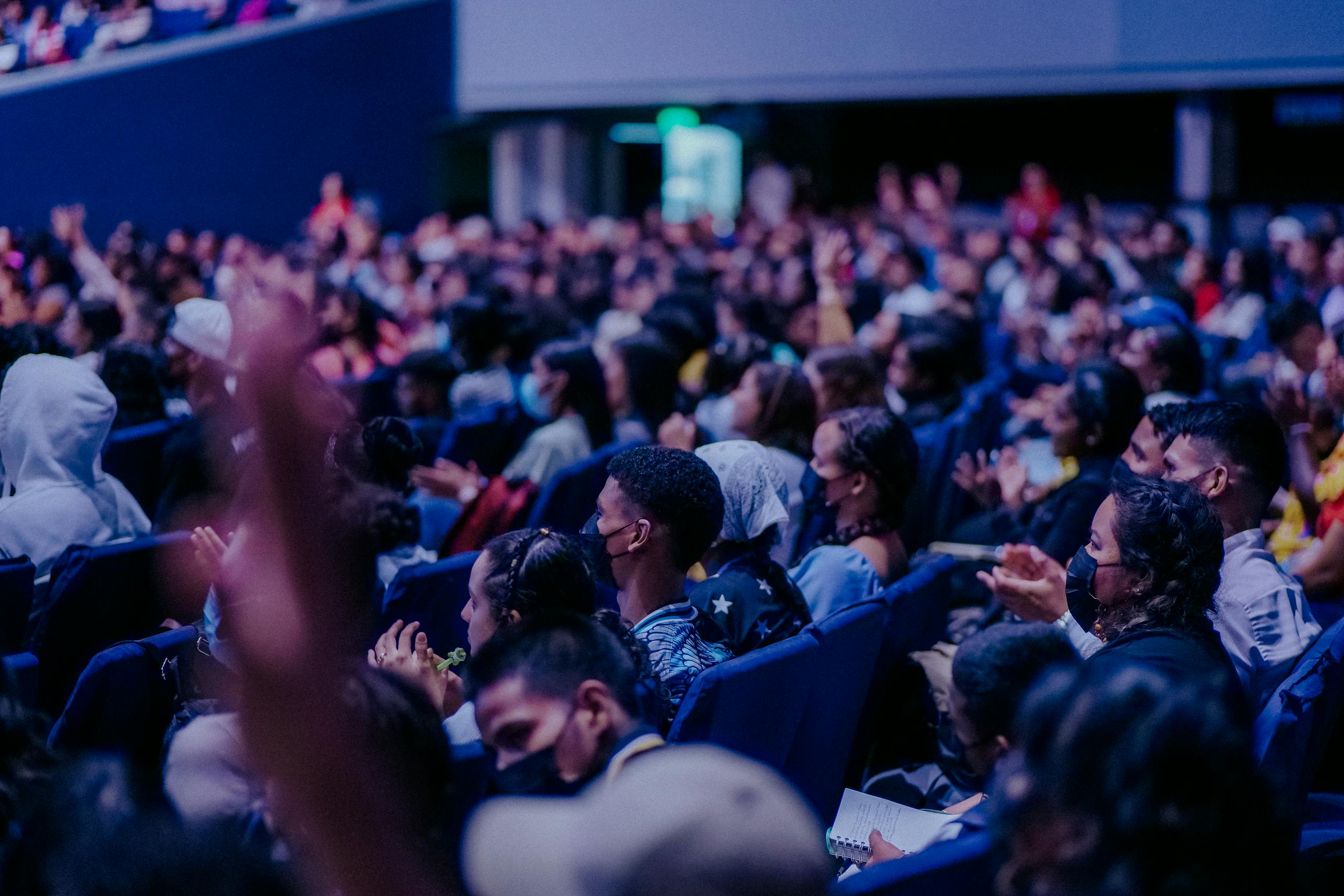 A large, diverse audience attentively watching a live event indoors, seated in rows.